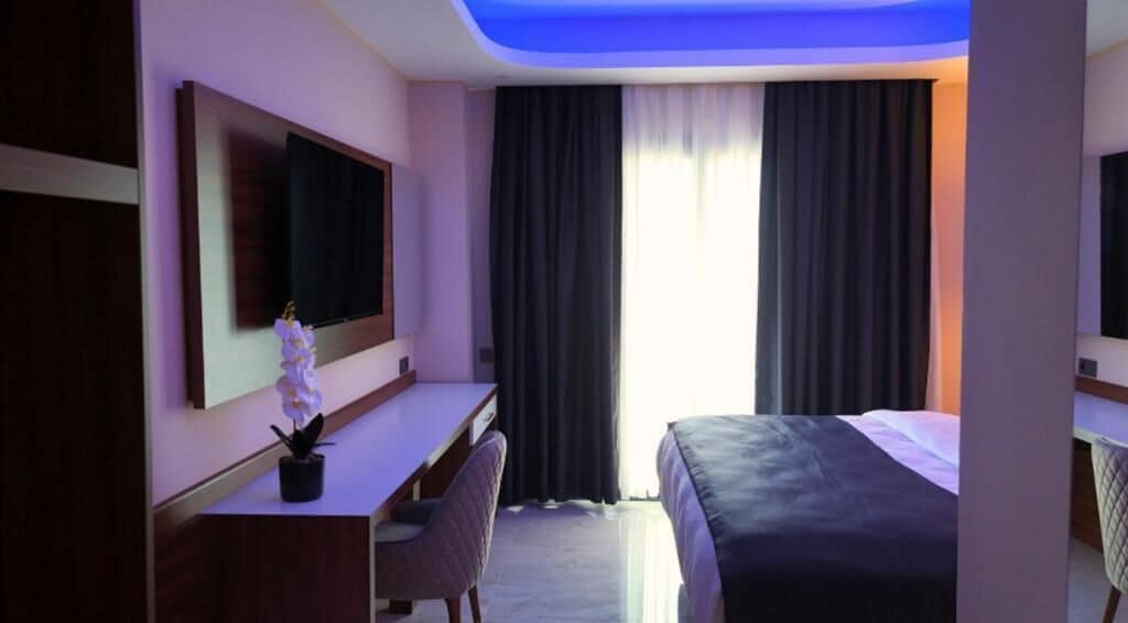Ein Hotelzimmer mit einem Bett, einem Schreibtisch, einem Stuhl, einem Fernseher und einem Fenster mit Vorhängen.