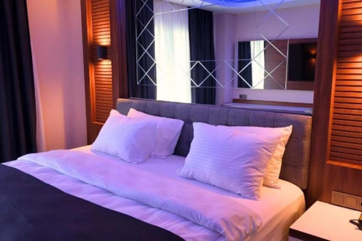 A modern hotel room with a large bed, a headboard with geometric patterns, and a bedside table with a lamp.