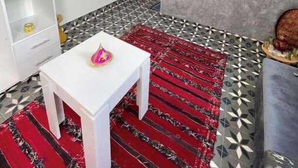 A modern living room with a white table, red patterned rug, and a TV mounted on a grey wall.