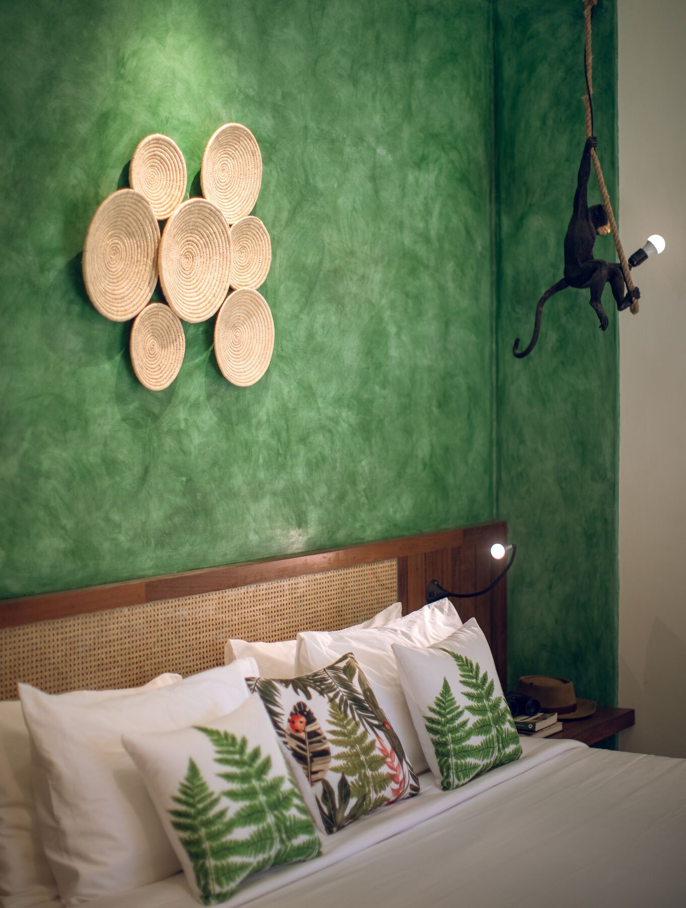 Een bed met witte lakens en decoratieve kussens, een geweven wandtapijt en een hanglamp.