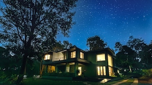 A modern two-story house with large windows, surrounded by trees, under a starry night sky. - Coorg Wild Walk- CGH Earth Saha (Virajpet)