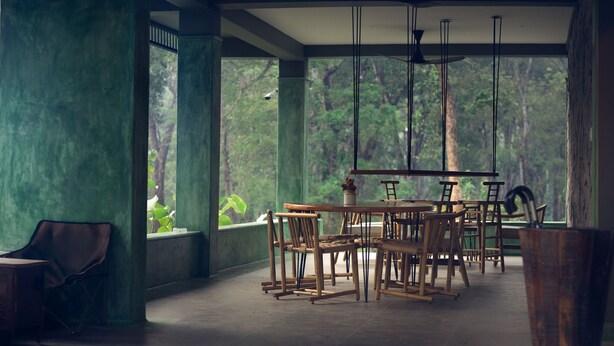 A conservatory with a dining area featuring wooden furniture and large windows. - Coorg Wild Walk- CGH Earth Saha (Virajpet)