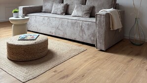 A modern loft-style living room with a sloped ceiling, a grey striped sofa, a small round ottoman, and a clear vase with pampas grass. - GIPFELGLÜCK - Apartment centrally located in Nesselwang - KÖNIGSKARTE  (Nesselwang)