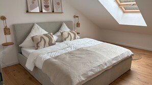 A bedroom with a sloped ceiling, a bed with white bedding and patterned pillows, a wooden floor, and a skylight. - GIPFELGLÜCK - Apartment centrally located in Nesselwang - KÖNIGSKARTE  (Nesselwang)