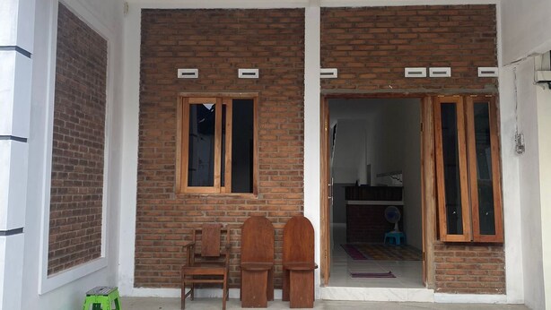Un edificio residencial con fachada de ladrillo, dos ventanas de madera y suelo de concreto.