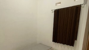 Una habitación pequeña con una cama individual, un colchón gris, una colcha a cuadros y una cortina marrón.
