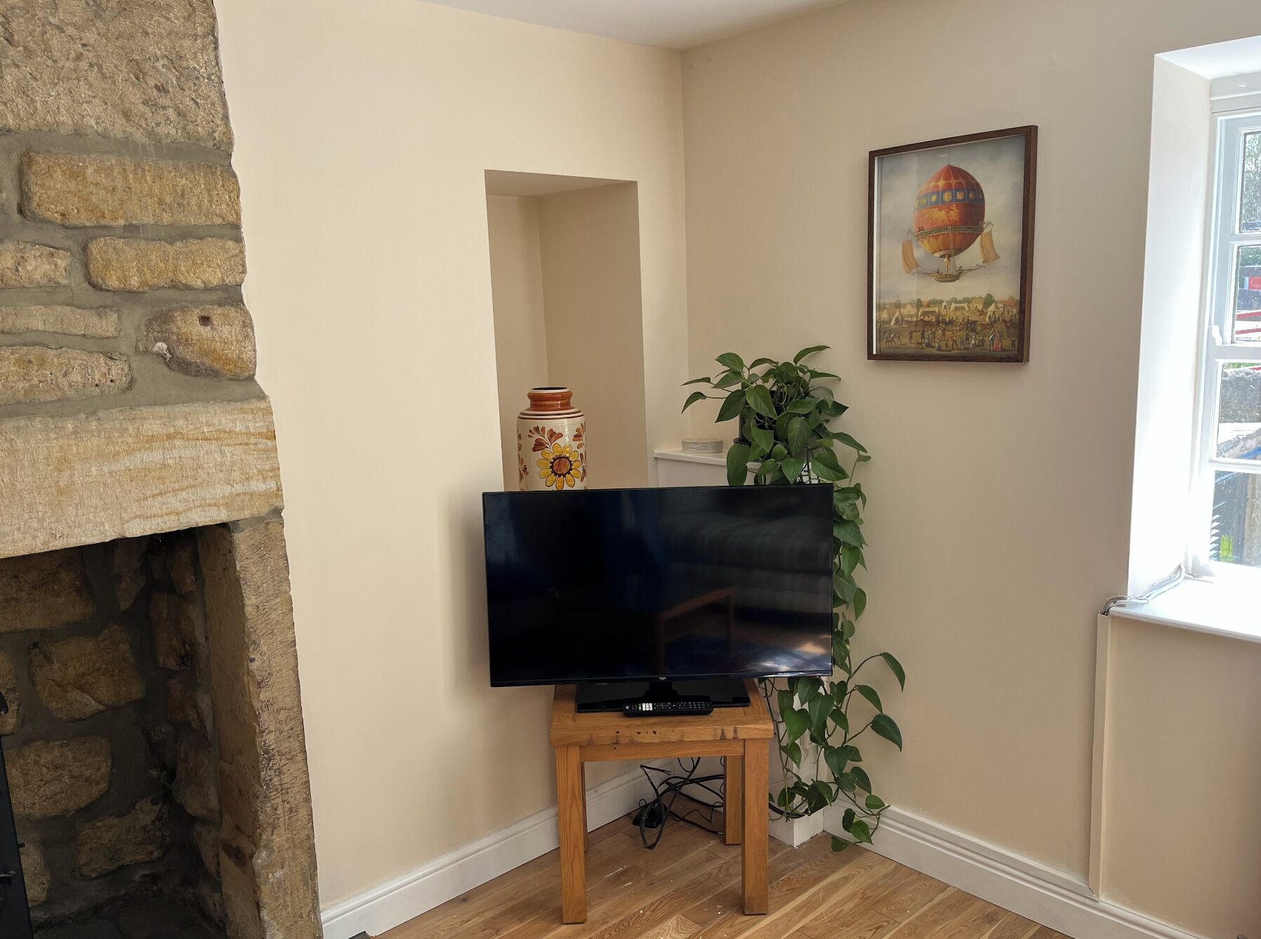 Un salon avec un téléviseur posé sur un meuble en bois, une plante en pot, un tableau et un mur en pierre.