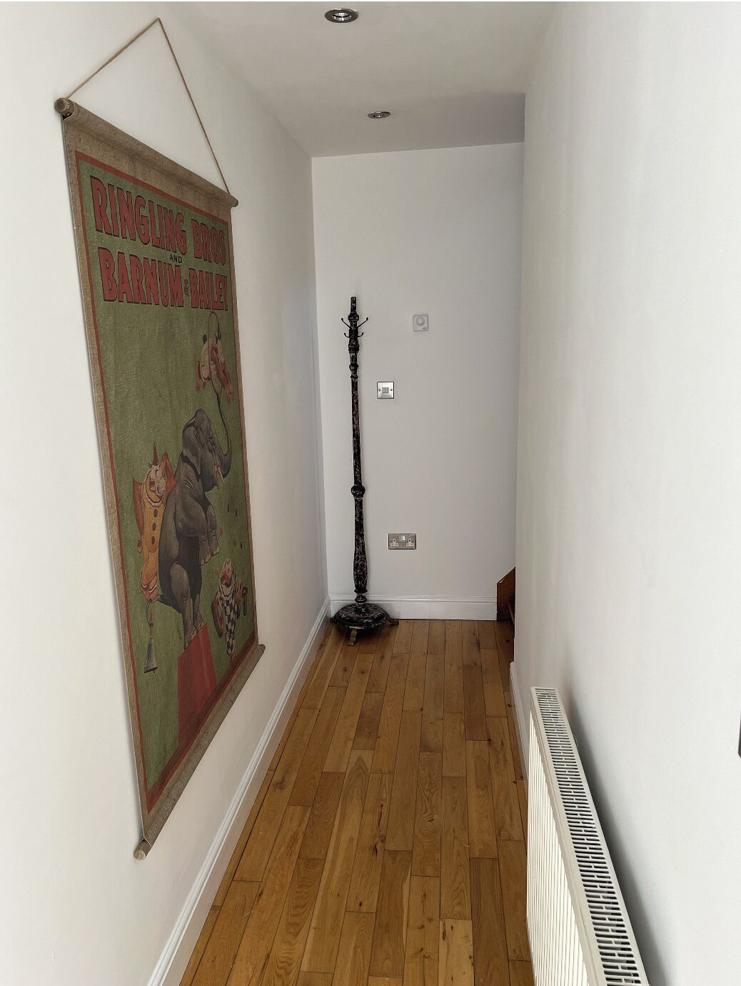 Un couloir étroit au plancher de bois, avec un radiateur et une affiche ancienne accrochée au mur.