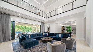 Ein geräumiges Wohnzimmer mit einem Ecksofa, einem Couchtisch und einem grauen Sessel. Durch die Glastüren ist ein Balkon mit Sitzgelegenheit einsehbar.