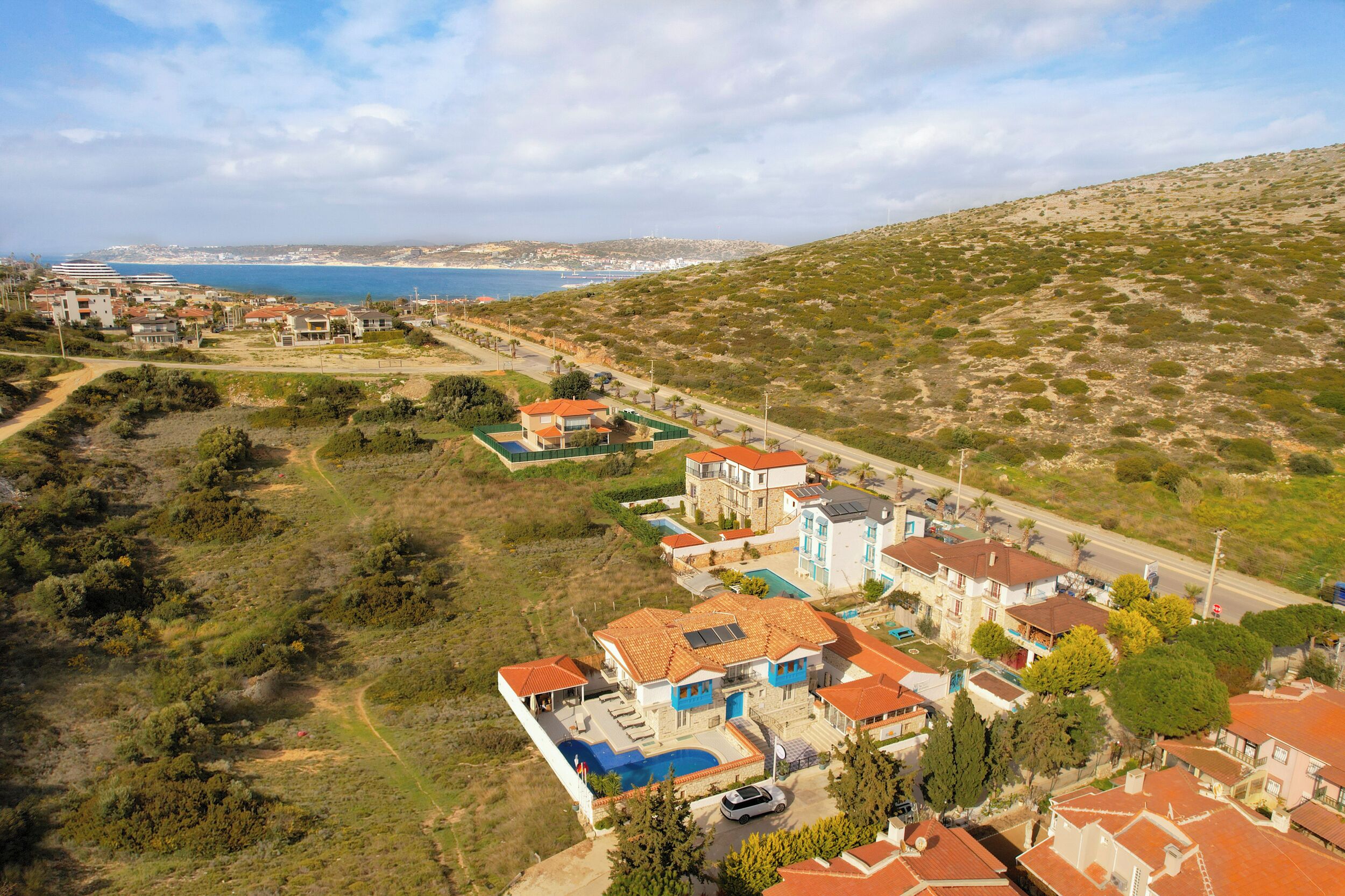 Vue aérienne d’un quartier résidentiel situé sur la côte, avec des maisons, une piscine et une route menant à la plage.