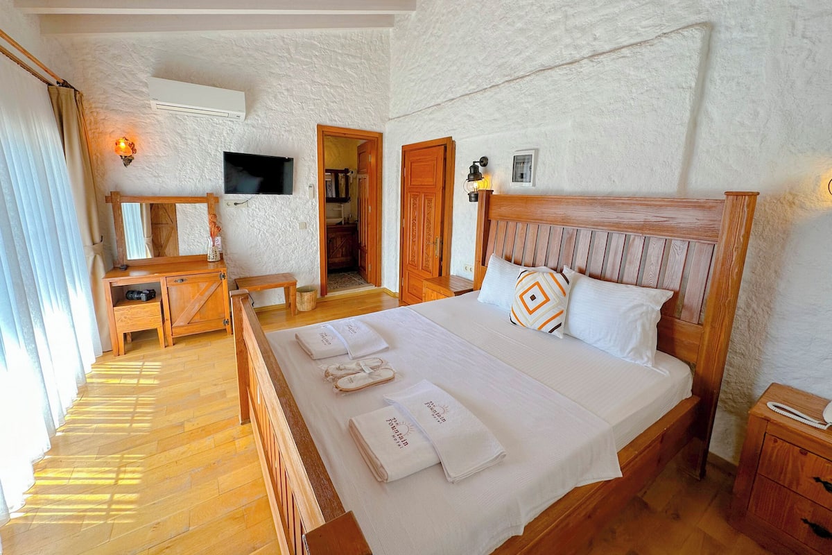 Een slaapkamer met een houten bed, een aan de muur bevestigde televisie, een nachtkastje van hout en een kledingkast van hout.