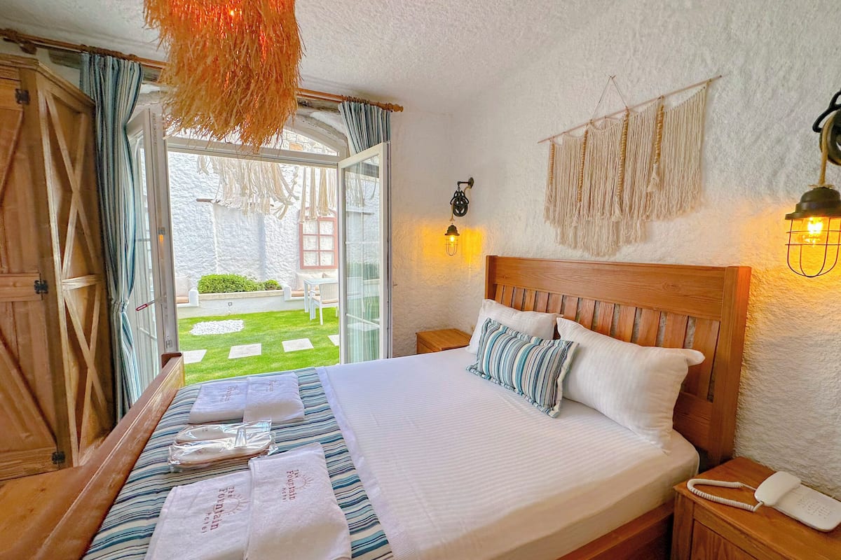 Een slaapkamer met een houten bed, wit beddengoed, een bedtafeltelefoon en uitzicht op een tuin door een open deur.