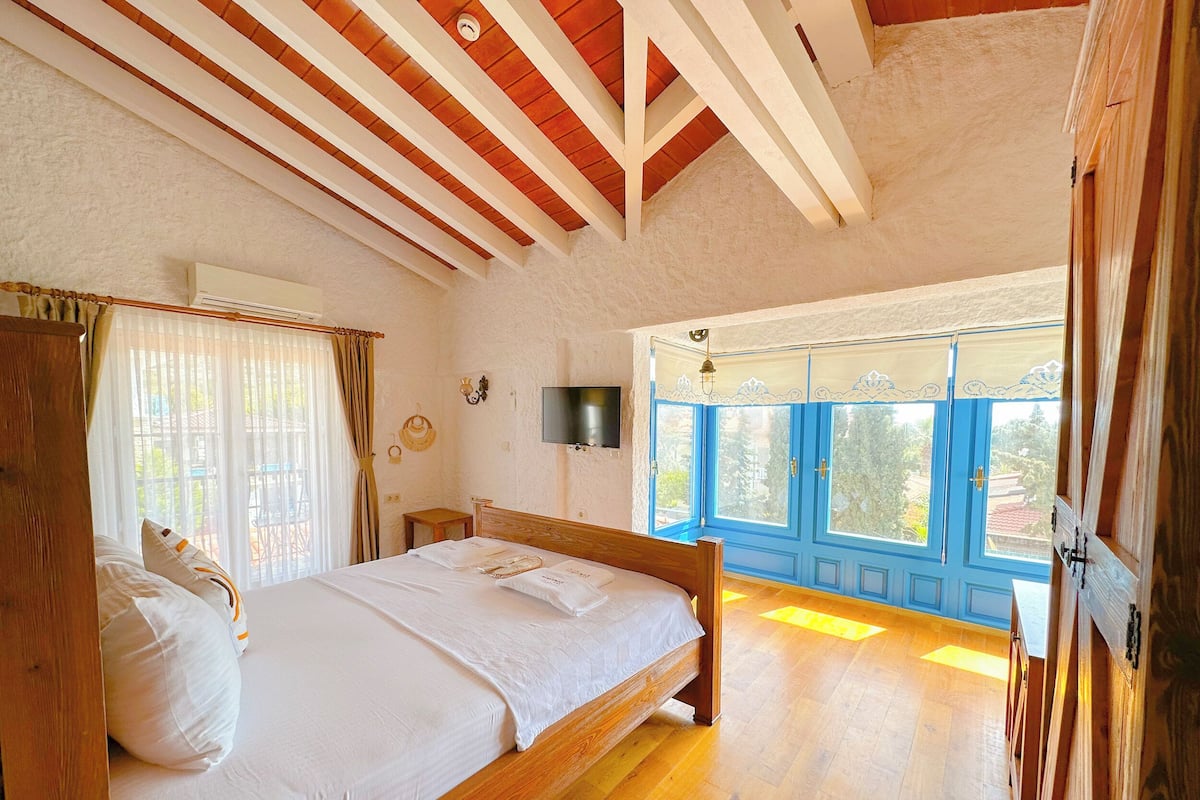 Een slaapkamer met een houten bed, een aan de muur bevestigde televisie en een raam met blauwe luiken.