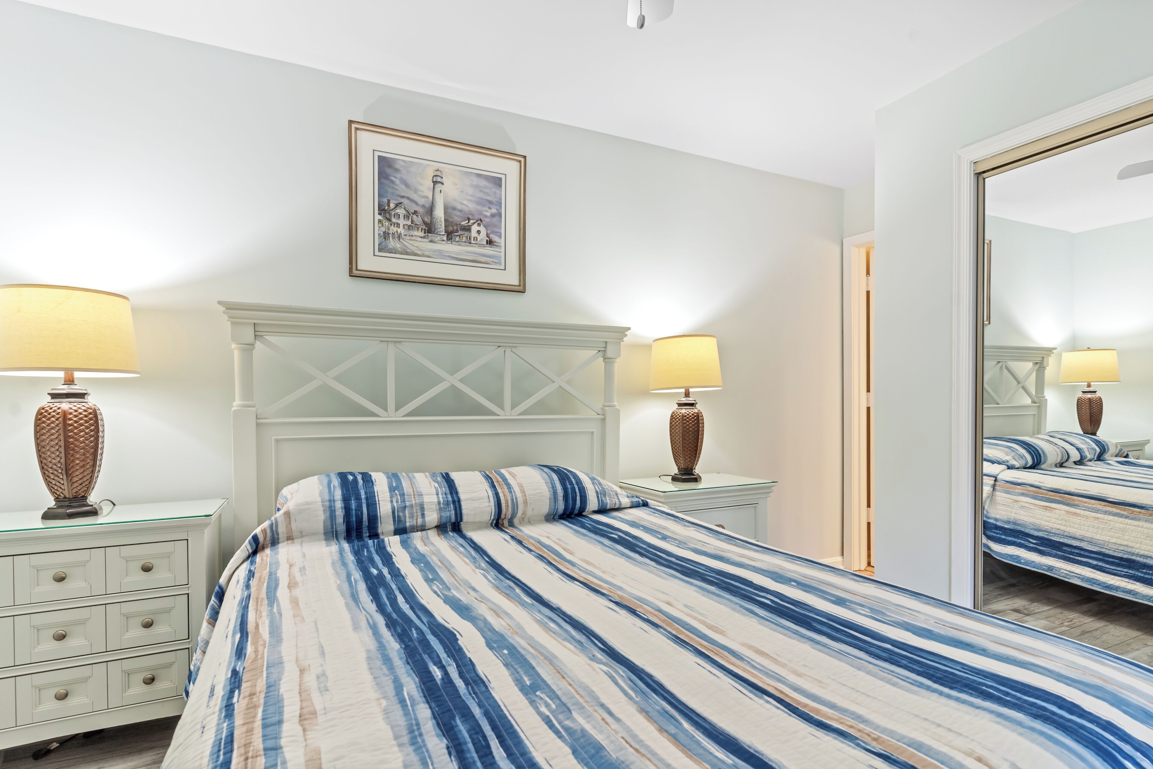 A bedroom with a bed, two bedside tables with lamps, a dresser, and a framed picture on the wall.