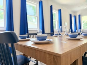 Comedor con cortinas azules, una mesa de madera y platos y fuentes azules y blancos a juego.