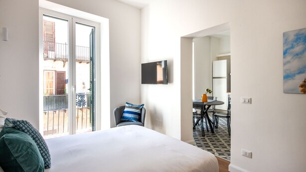 A hotel room with a bed, a chair, a TV, and a balcony with a view of buildings. - Ci' Capo 2 by Wonderful Italy (Palermo)