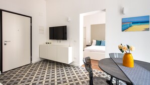A modern hotel room with a dining area, a TV mounted on the wall, and a painting of a beach scene. - Ci' Capo 2 by Wonderful Italy (Palermo)