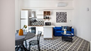 A modern kitchen with white cabinets, a microwave, and a coffee machine. There is a dining area with a table and chairs, and a blue sofa in the living area. - Ci' Capo 2 by Wonderful Italy (Palermo)