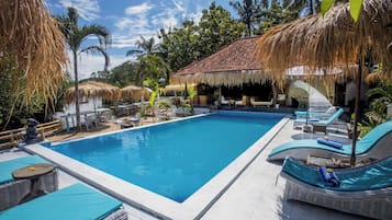 Una piscina rectangular con sillas de descanso y una estructura de techo de paja.