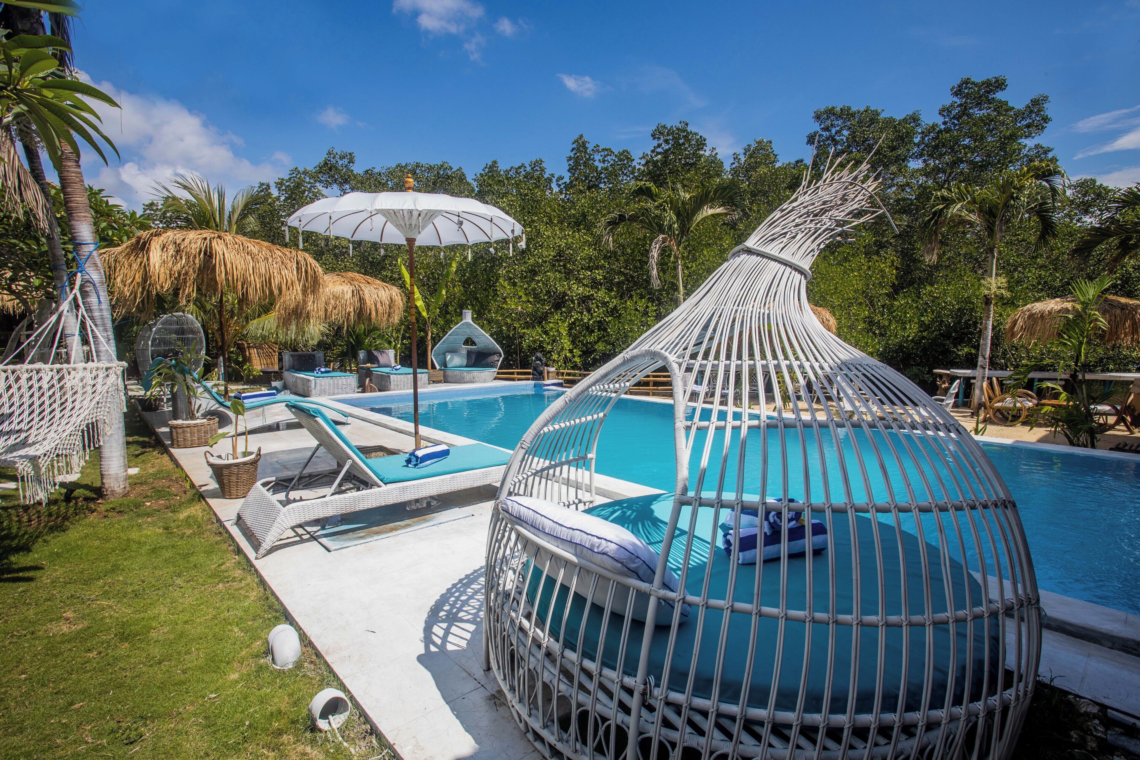 A pool area with a thatched-roof structure, a hanging chair, and a white umbrella.