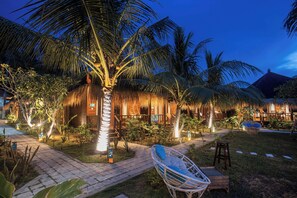 Un resort tropical con edificios de techo de paja, un sendero pavimentado y zonas de estar al aire libre.