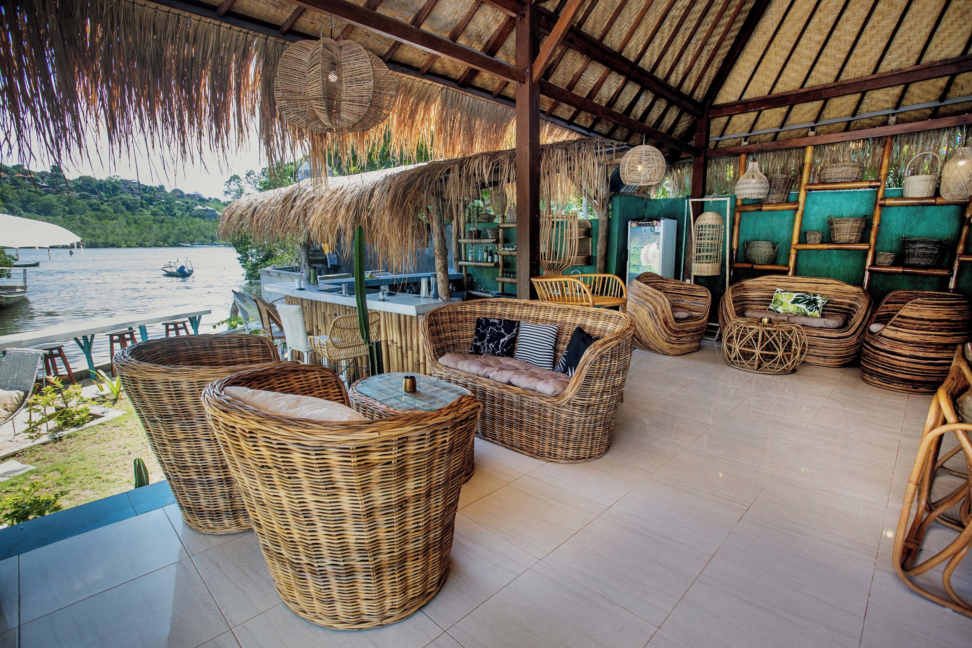 A thatched-roof outdoor seating area with wicker furniture and a view of the water.