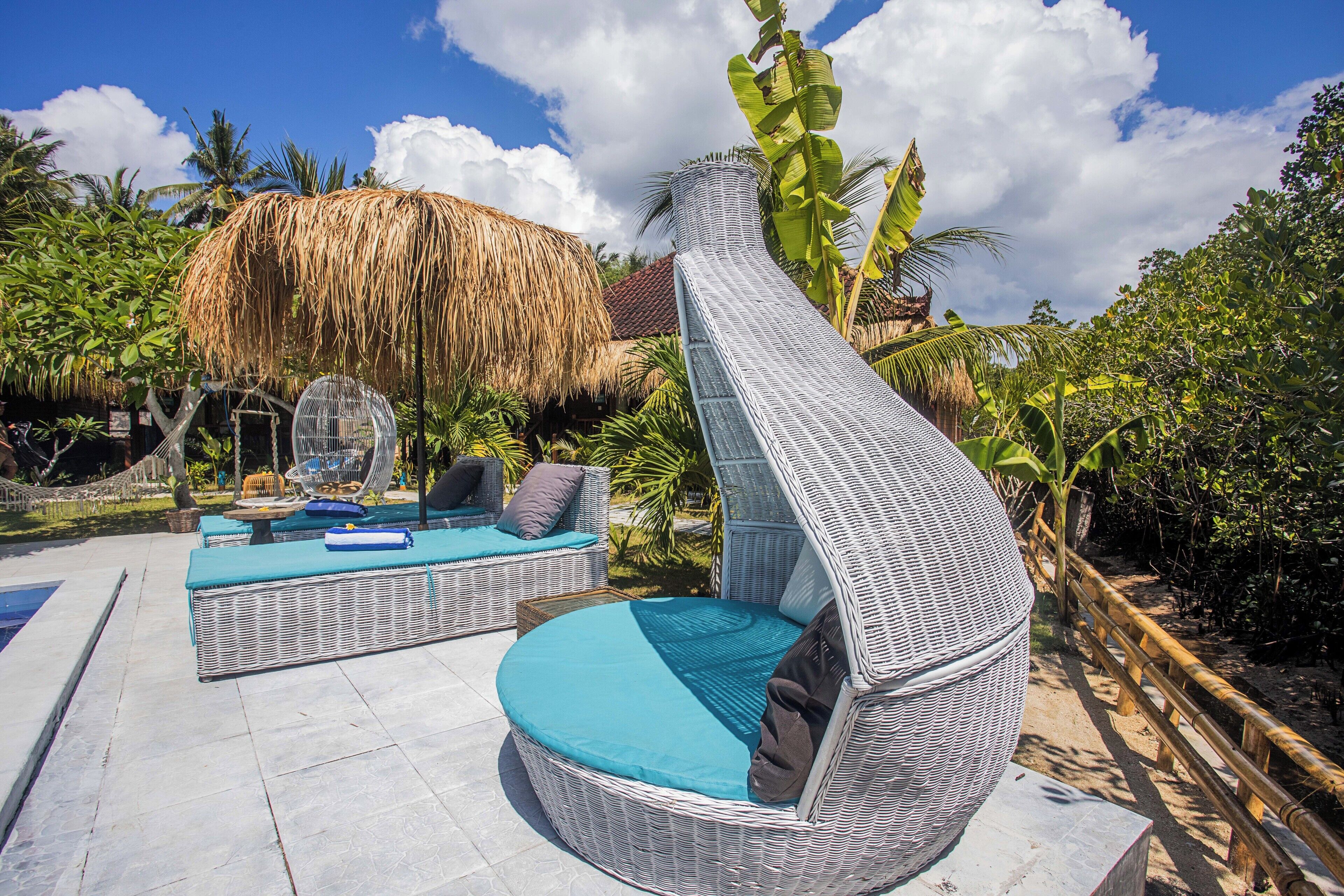 A wicker lounge chair with a curved design, a thatched-roof structure, and a pool area with lounge furniture.
