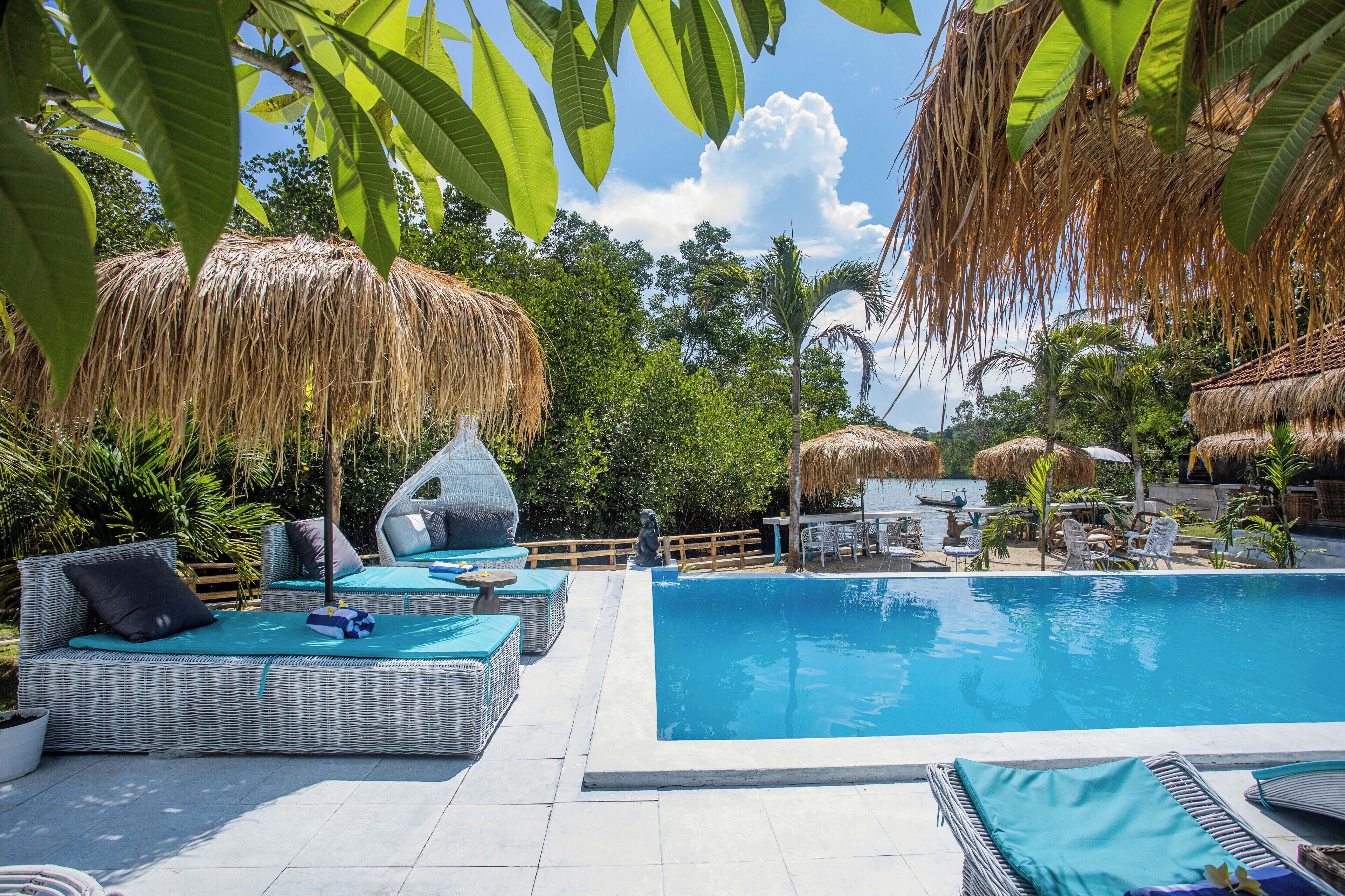 A pool area with wicker furniture and thatched umbrellas.