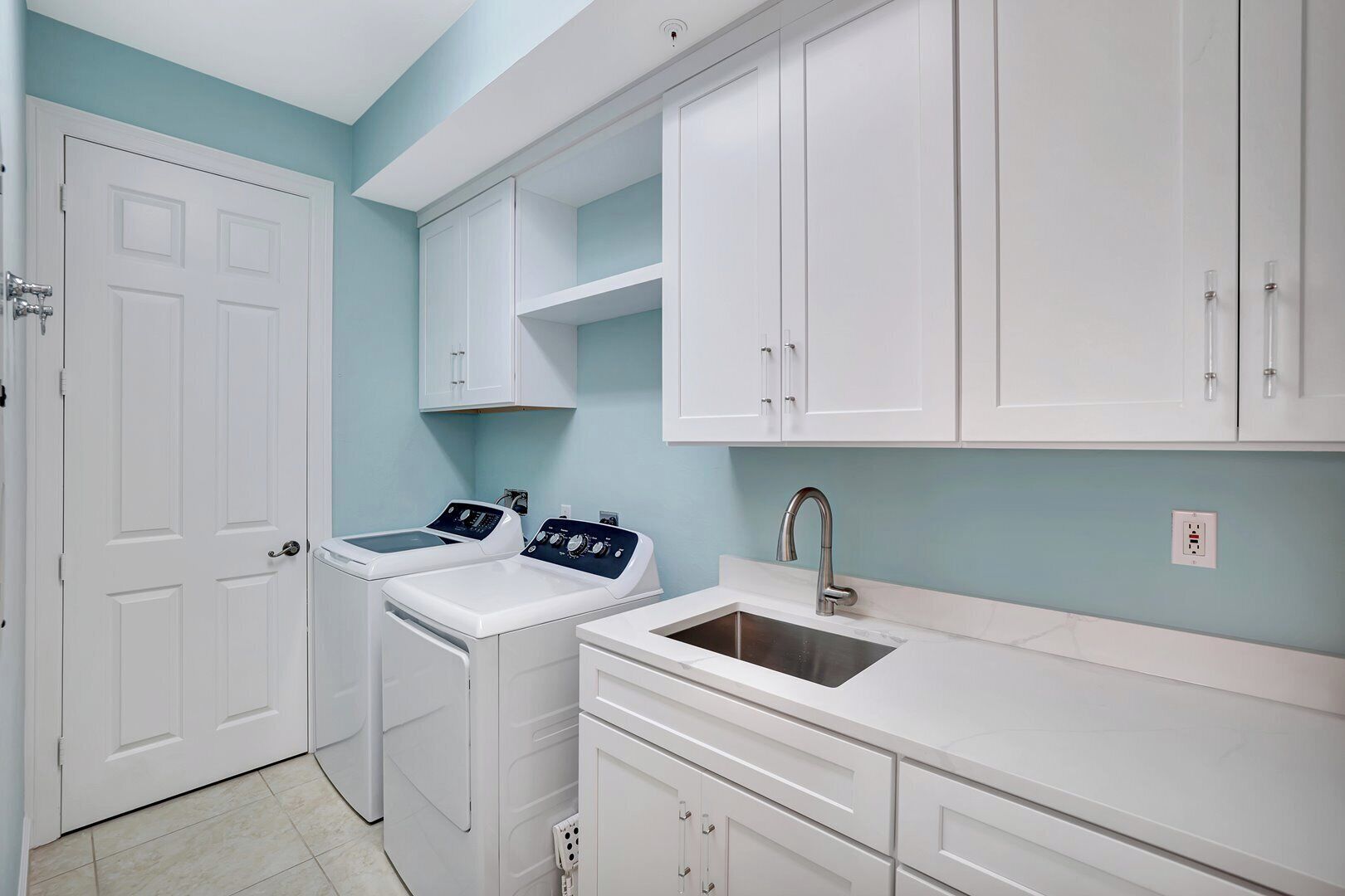 A laundry room with two washing machines, a sink, and white cabinets.