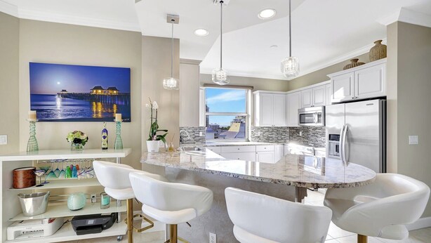 A modern kitchen with a large island, white bar stools, and a view of the city. - Regatta - WALK TO THE BEACH (Naples)