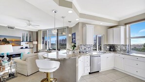 A modern kitchen with a large island, white cabinetry, and a view of the city. - Regatta - WALK TO THE BEACH (Naples)
