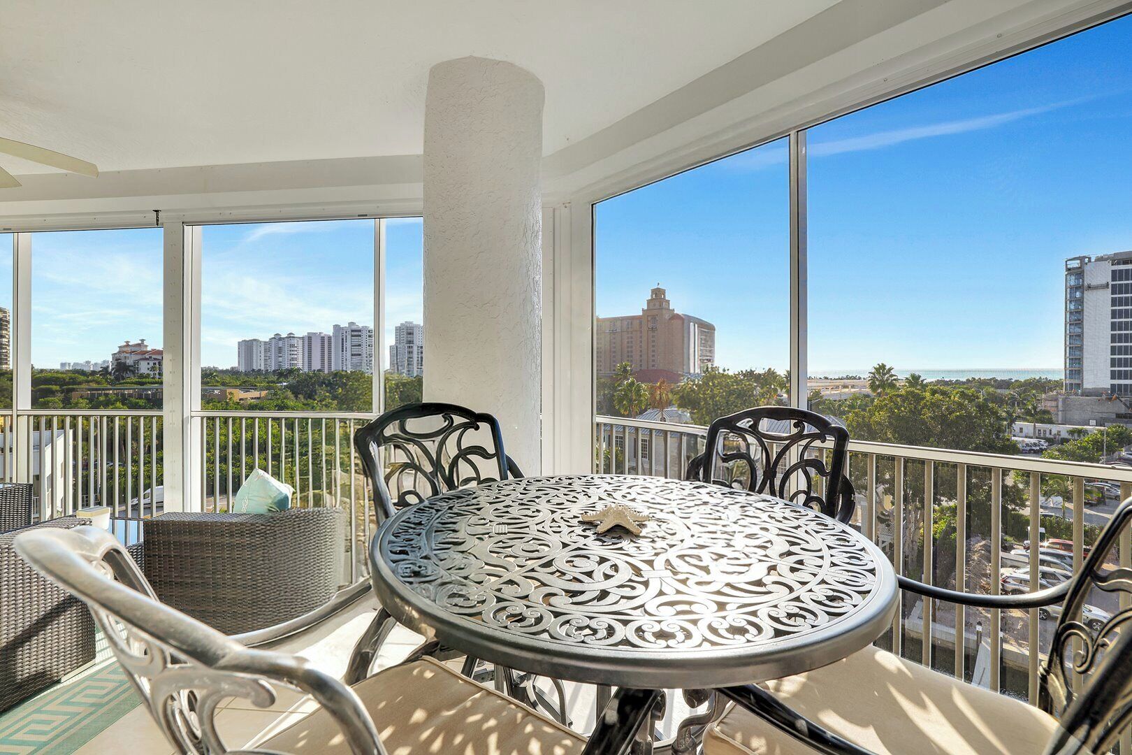 A balcony with a round table and chairs, large windows offering a city view.