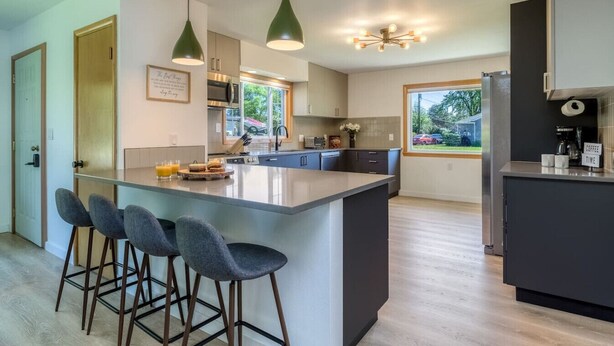 Una cocina moderna con una isla central, taburetes de bar, iluminación colgante y vistas al exterior.