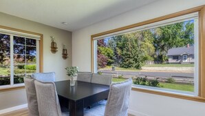 Comedor con una mesa oscura y sillas tapizadas en gris, amplias ventanas con vista a un barrio residencial.