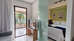 Une chambre d’hôtel moderne avec un balcon, une télévision, un lit recouvert d’une courtepointe bleue et deux tableaux encadrés au mur.