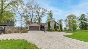 A residential driveway leading to a garage, surrounded by a gravel area and a grassy lawn. - Cozy Lakefront Home, Minutes from Lake MI, 2 Bedrooms, 2 Bathrooms. Sleeps 6 (Manistee)