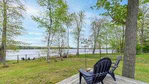 A deck with a chair and a fire pit overlooking a lake, surrounded by trees. - Cozy Lakefront Home, Minutes from Lake MI, 2 Bedrooms, 2 Bathrooms. Sleeps 6 (Manistee)