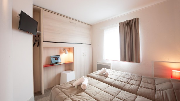 A hotel room with two beds, a TV, a desk with a laptop, a window with curtains, and a radiator. - Bayside Apartment in Bleriot-plage (Frethun)