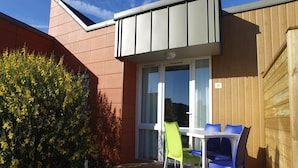 A patio with a table and chairs, a wooden fence, and a bush with yellow flowers. - Bayside Apartment in Bleriot-plage (Frethun)