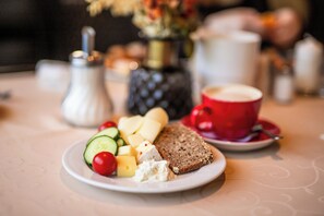 Une assiette contenant du fromage, du concombre, des tomates et du pain, posée sur une table avec une tasse et une soucoupe.