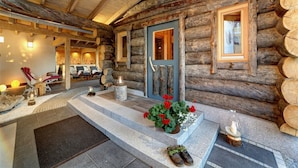 A log cabin with a stone staircase leading to a wooden door, a seating area with a red chair, and a small table with candles. - Wellnesshotel Hofbräuhaus (Bodenmais)