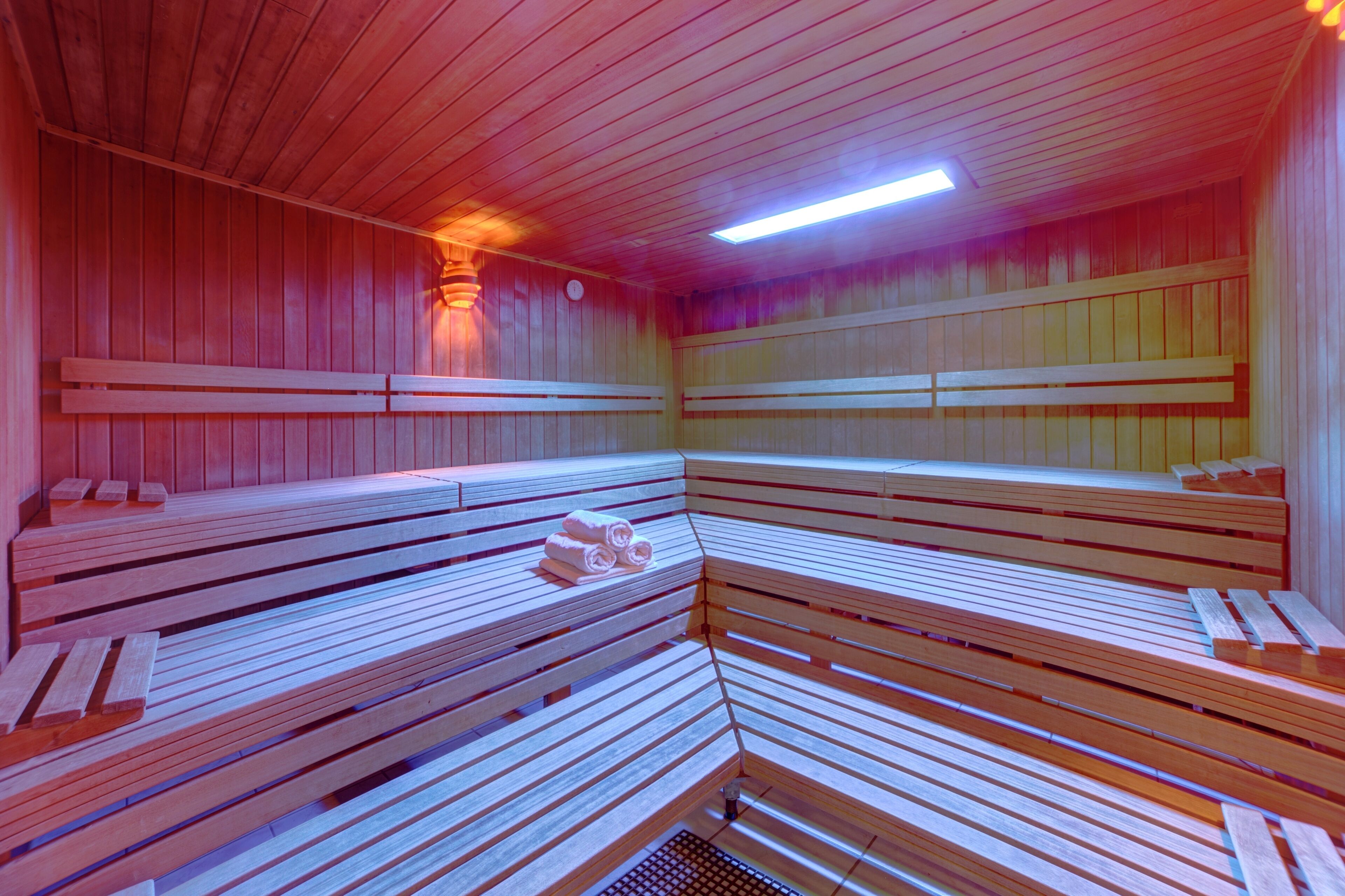 A sauna with wooden benches arranged in a semi-circular pattern, a ventilation system, and a ceiling light.