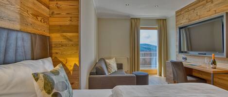 Une chambre d’hôtel avec un mur en bois, un lit, un canapé, un bureau avec une télévision et une vue sur l’extérieur.