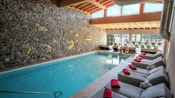 Una piscina con paredes de piedra y vigas de madera, rodeada de sillas de descanso con toallas.