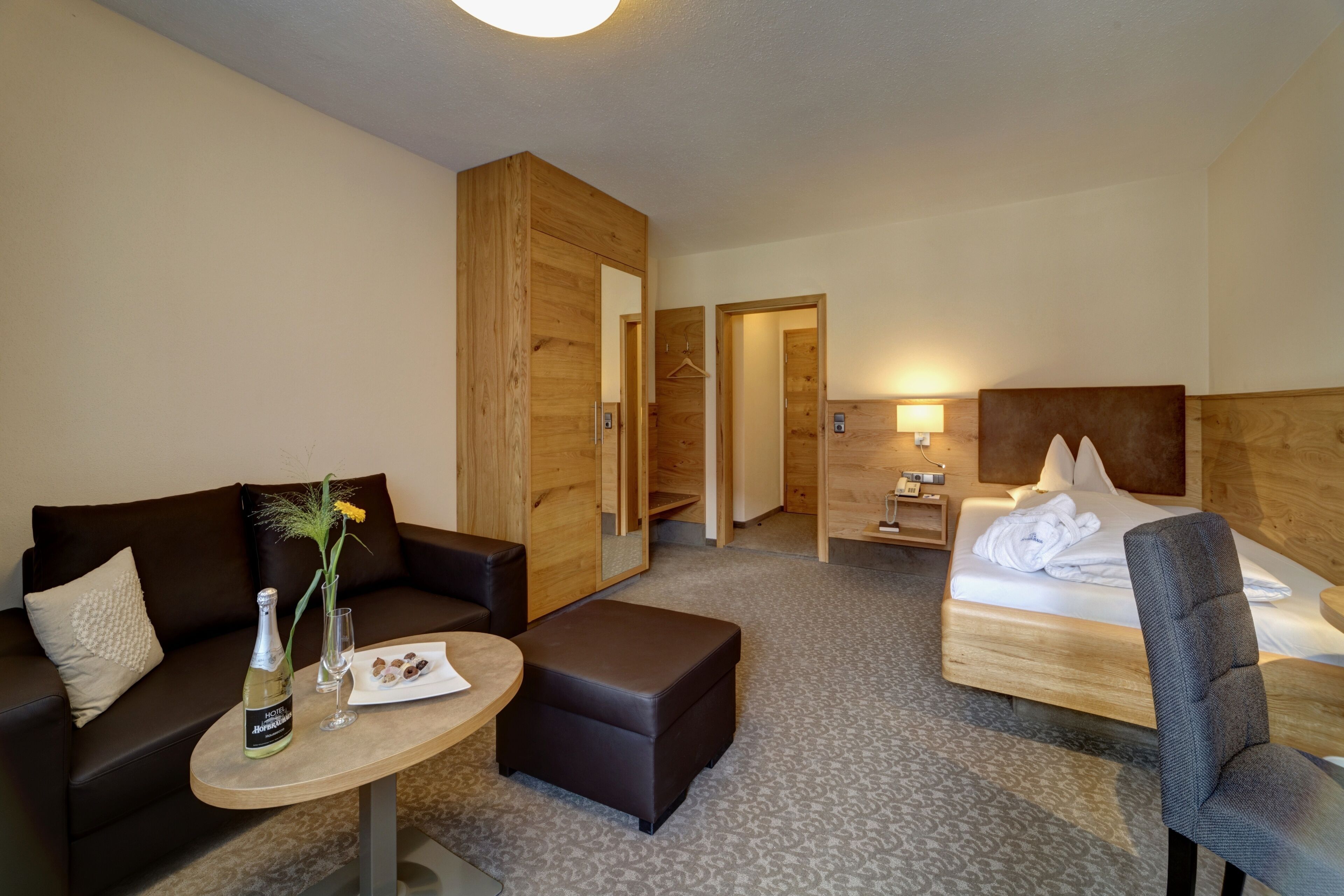 Ein Hotelzimmer mit einem Bett, einer Couch, einem kleinen Tisch mit einer Flasche und Gläsern sowie einem Holzschrank.