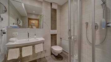 Een moderne badkamer met een glazen douchecabine, een witte wastafel met spiegel, en een toilet.