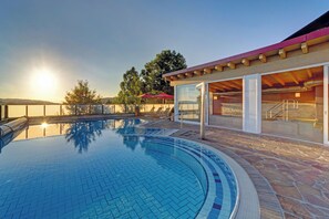Une piscine avec une terrasse en pierre, un patio couvert et une vue sur le coucher de soleil.