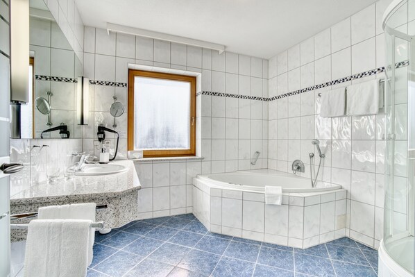 Un baño moderno con una bañera grande, una zona de ducha independiente y un tocador con lavabo y espejo.