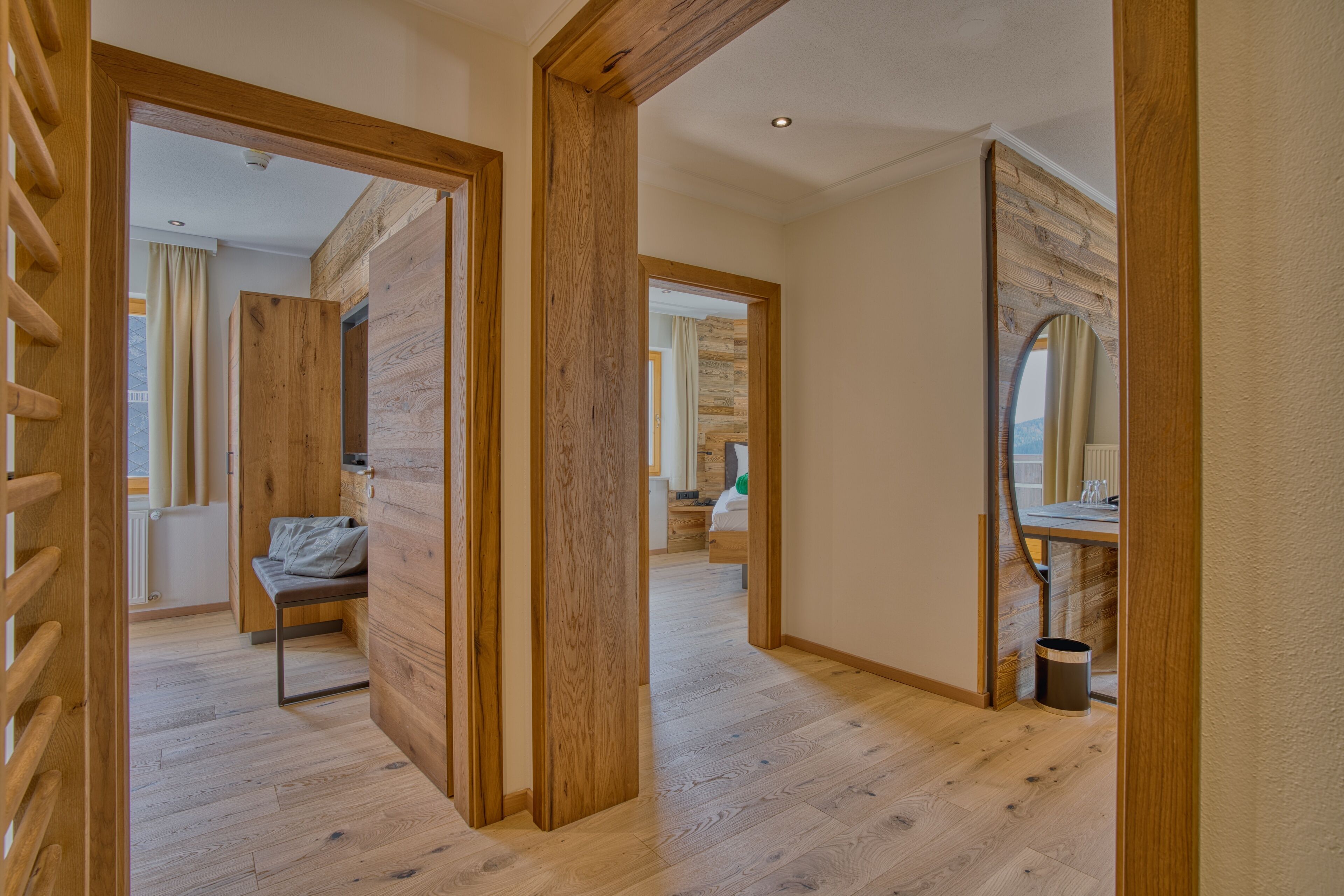A hallway with wooden flooring and walls, leading to a bedroom with a bed and a bathroom with a mirror and sink.