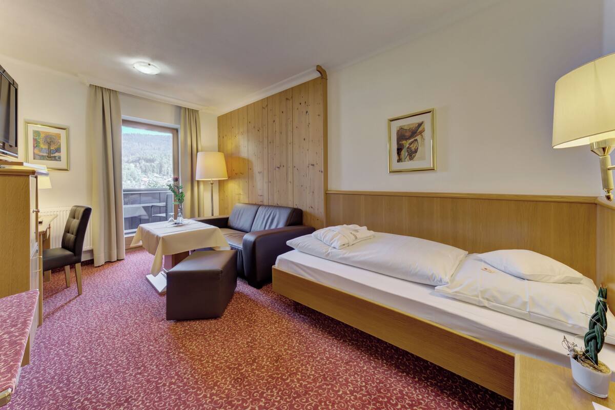 Une chambre d’hôtel avec un lit, un canapé, une petite table, une chaise, une lampe et une fenêtre avec des rideaux.